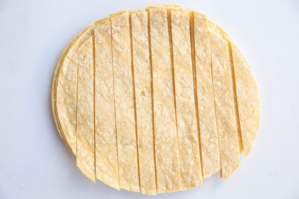 Stack of corn tortillas on a cutting board, sliced into strips.