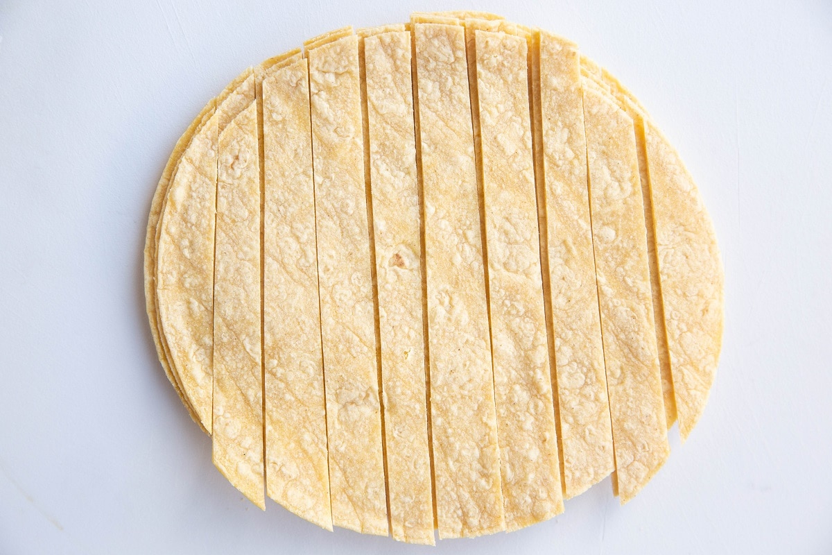 Stack of corn tortillas on a cutting board, sliced into strips.