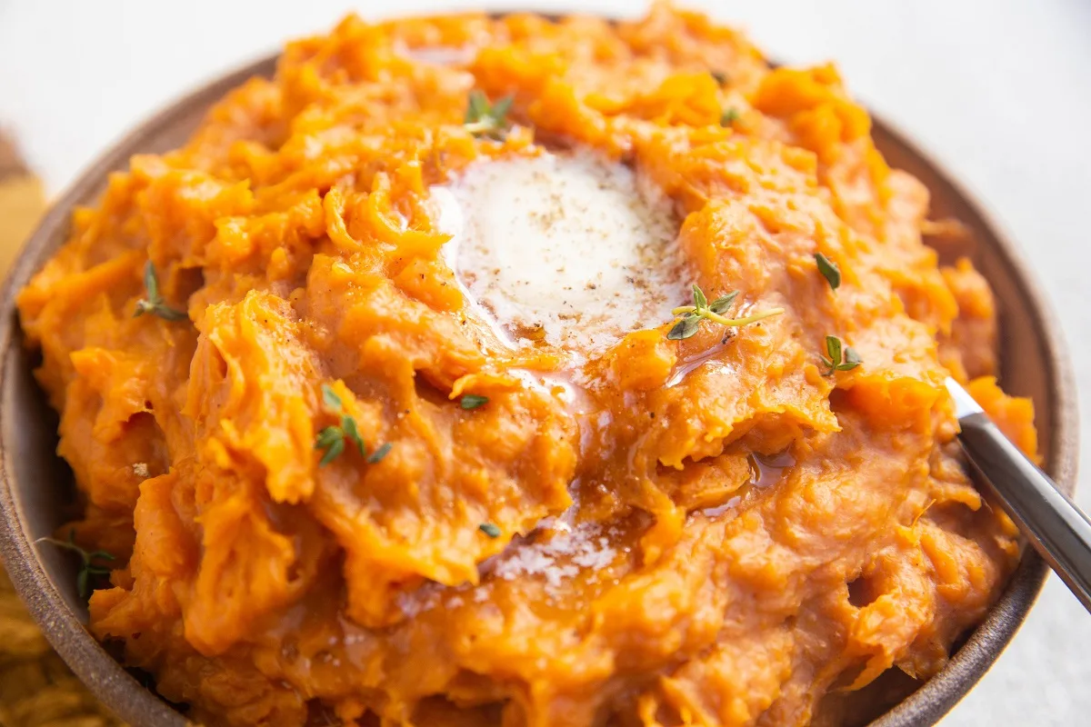 Horizontal photo of mashed sweet potatoes in a bowl with butter on top.