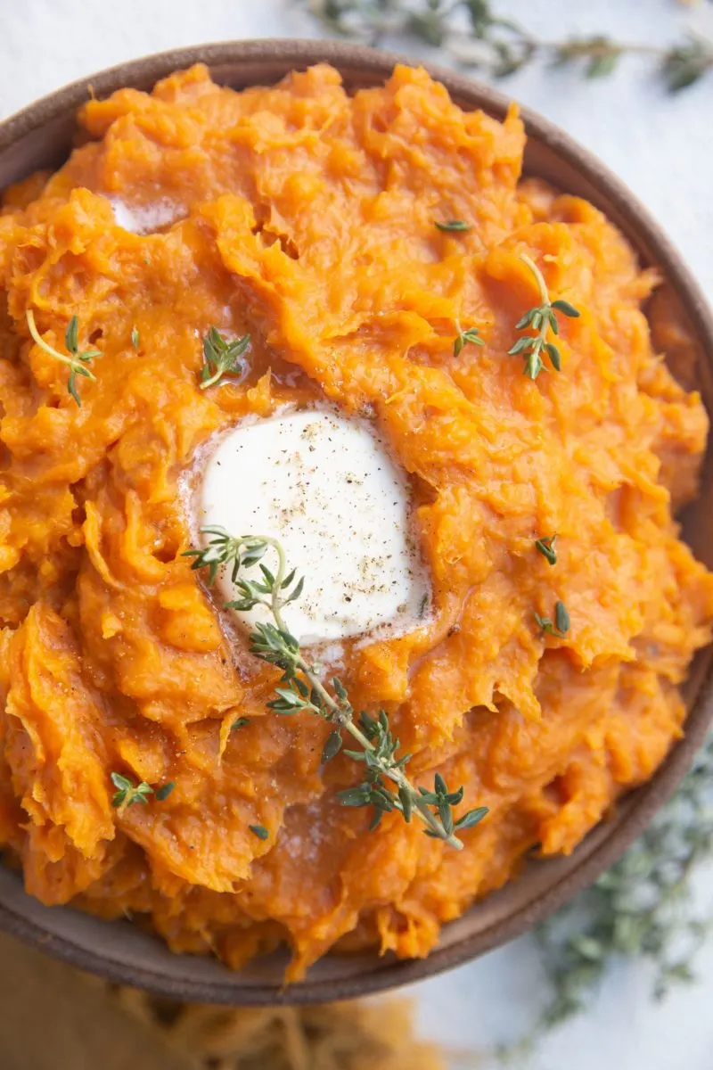 Close up top down photo of mashed sweet potatoes in a bowl with melted butter and fresh thyme on top.