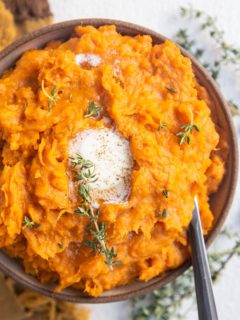 Bowl of mashed sweet potatoes with melted butter on top and a serving spoon.