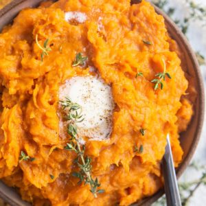 Bowl of mashed sweet potatoes with melted butter on top and a serving spoon.