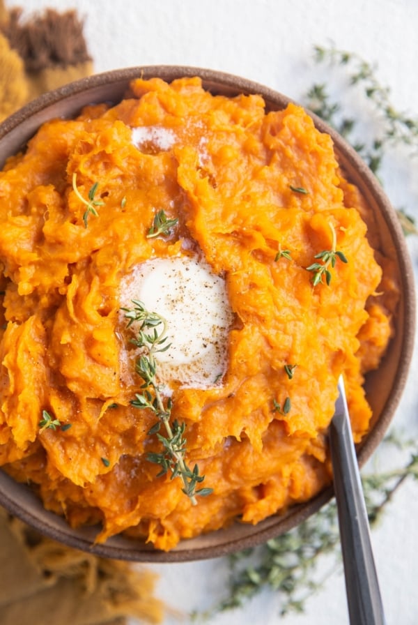 Bowl of mashed sweet potatoes with melted butter on top and a serving spoon.
