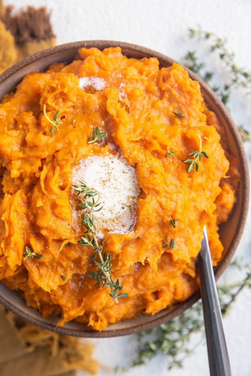 Bowl of mashed sweet potatoes with melted butter on top and a serving spoon.