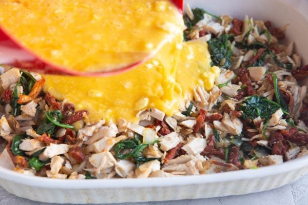 Egg mixture being poured over the ingredients in the casserole dish.