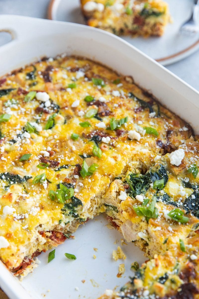 Casserole dish of leftover turkey breakfast casserole with one piece taken out and a plate with a slice of breakfast casserole in the background.