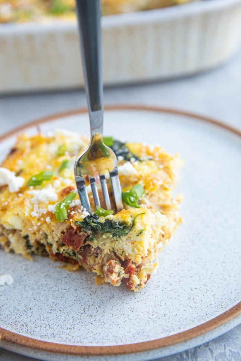 Slice of breakfast casserole on a plate with a fork taking a bite out.