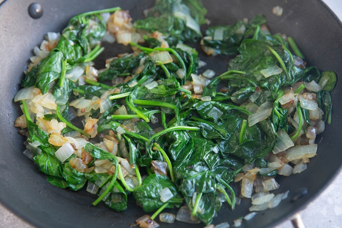 Onions, spinach, and garlic cooking in a skillet.