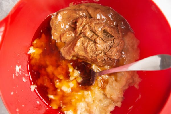 Mashed bananas in a mixing bowl with almond butter and pure maple syrup, ready to be mixed together.