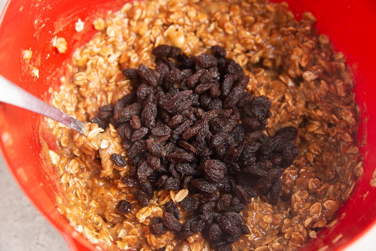 Oatmeal Cookie dough in a mixing bowl with raisins on top, ready to be mixed in.