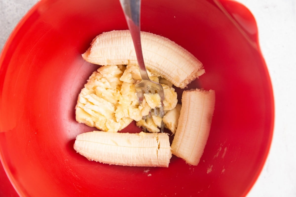Mashed bananas in a red mixing bowl.