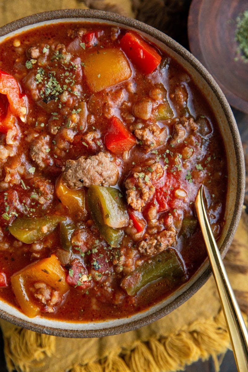 Close up top down photo of bowl of stuffed pepper soup with a gold spoon on top of a golden napkin.