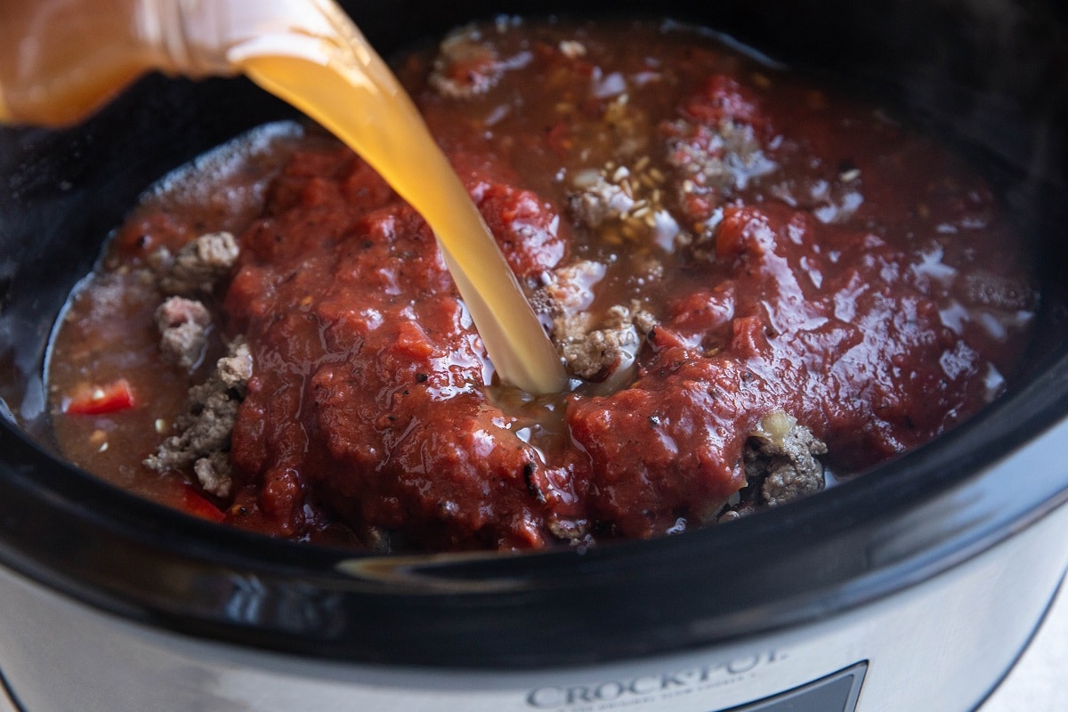 Pouring chicken broth in a crock pot.