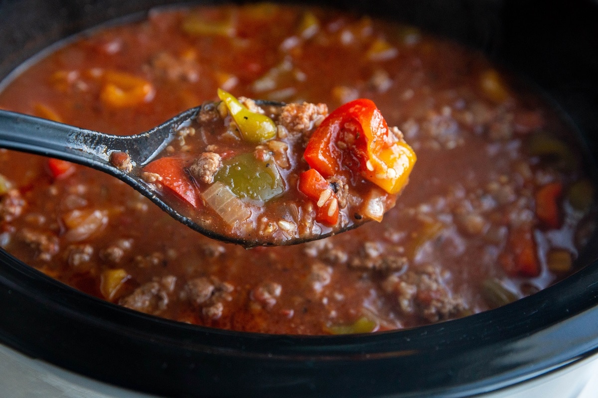 Horizontal image of a crock pot full of ground beef and pepper soup with a scoop of soup in a ladel.