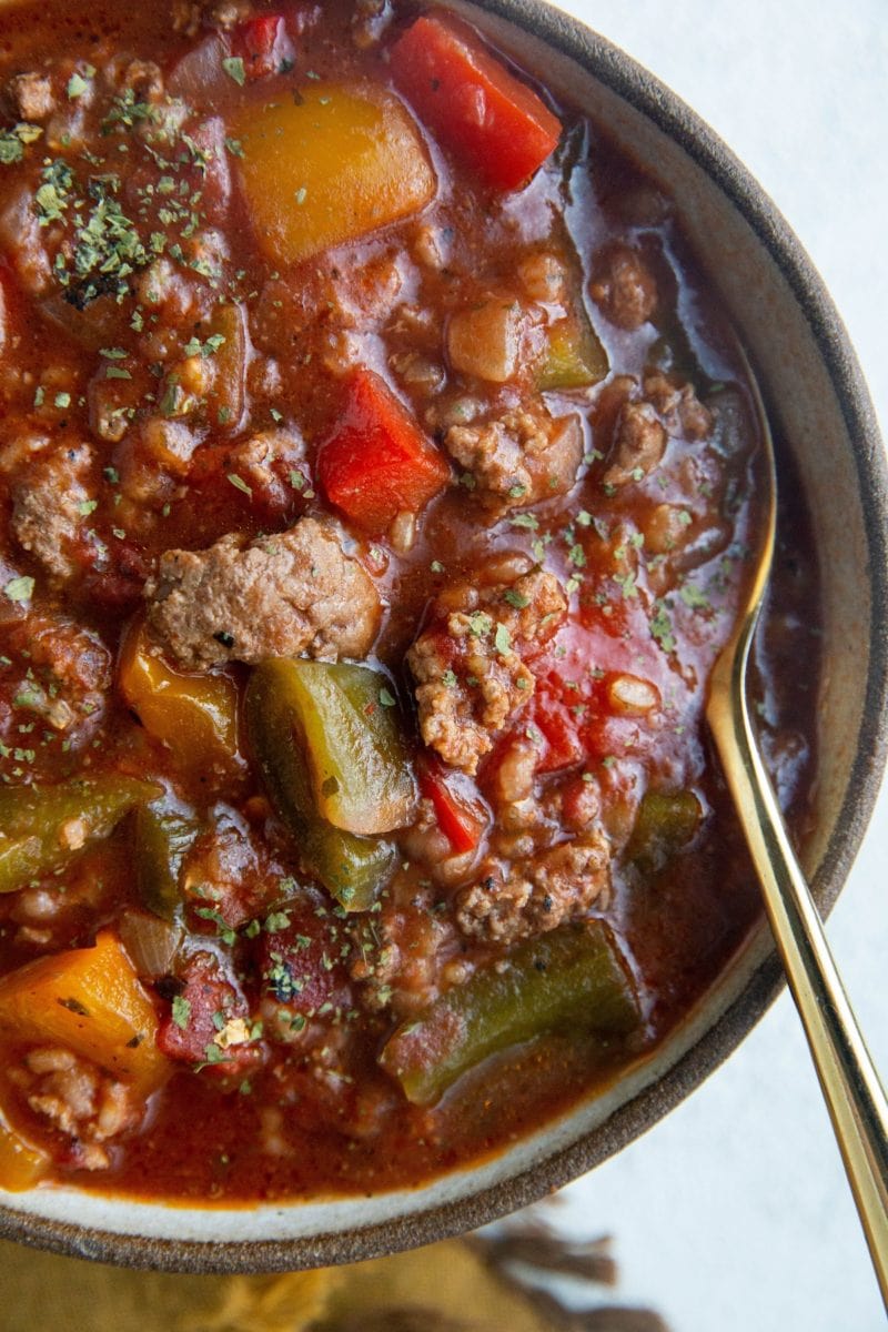 Top down close up photo of a bowl of Slow Cooker Stuffed pepper Soup with a gold spoon.