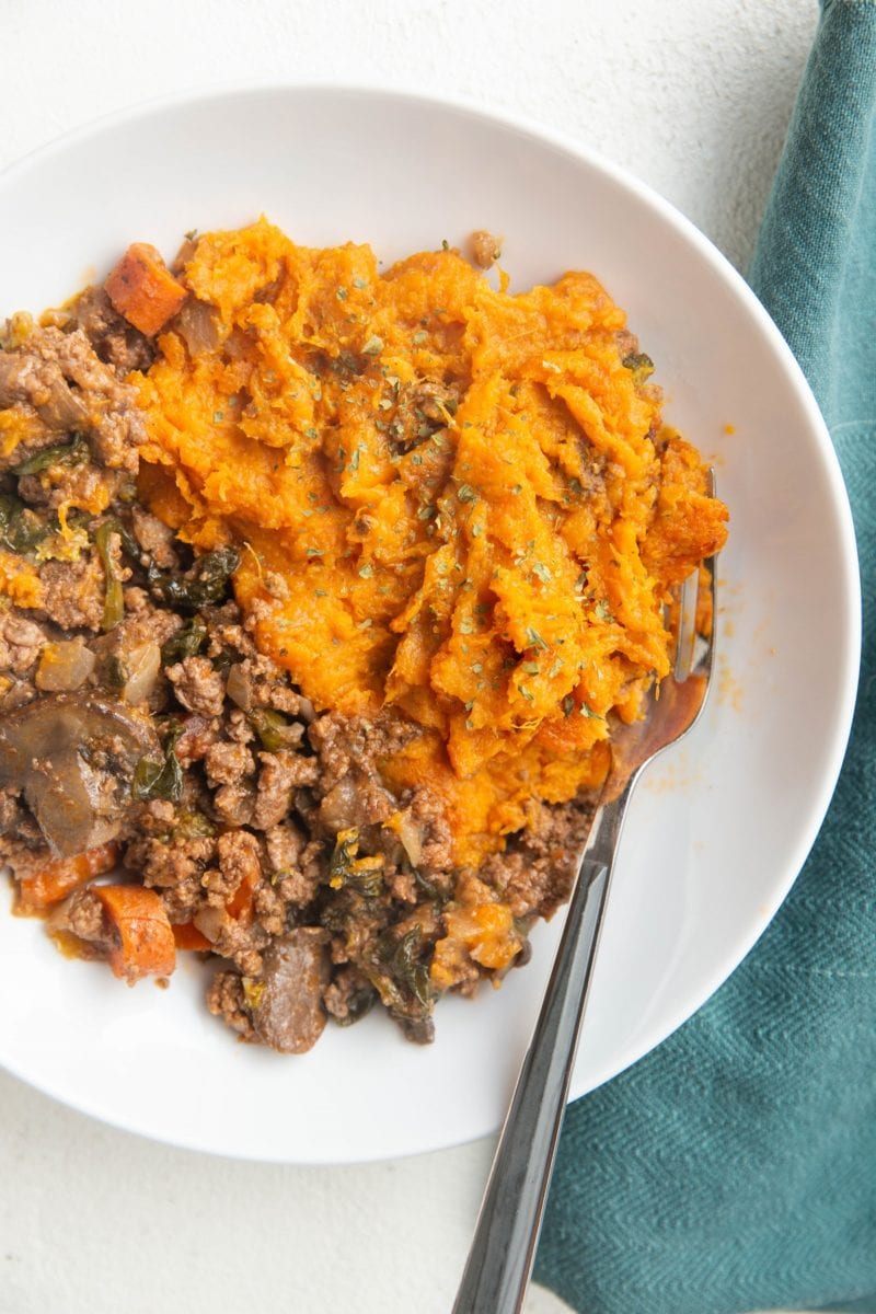 White bowl with mashed sweet potatoes and ground beef mixed with vegetables. Sweet potato shepherd's pie served in a bowl.