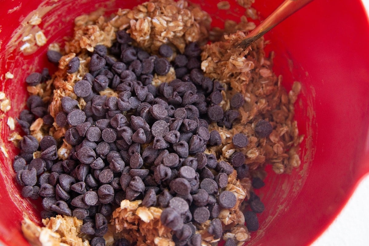 Chocolate chips on top of oatmeal cookie dough ready to be mixed in.