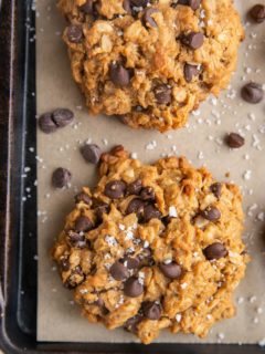 Baked peanut butter oatmeal cookies on a parchment lined baking sheet sprinkled with sea salt and extra chocolate chips.