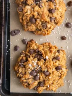 Baked peanut butter oatmeal cookies on a parchment lined baking sheet sprinkled with sea salt and extra chocolate chips.