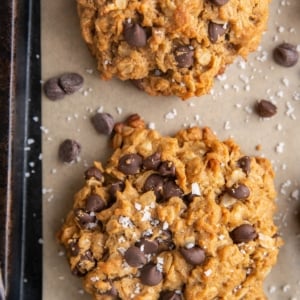 Baked peanut butter oatmeal cookies on a parchment lined baking sheet sprinkled with sea salt and extra chocolate chips.