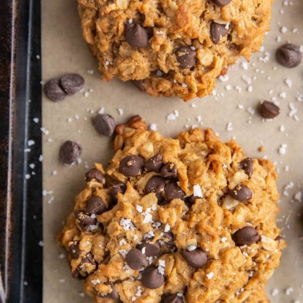 Baked peanut butter oatmeal cookies on a parchment lined baking sheet sprinkled with sea salt and extra chocolate chips.