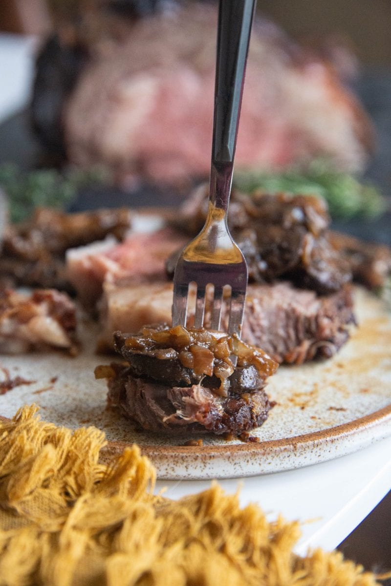 Vertical image of a close up shot of a forkful of prime rib, mushrooms, and onions.