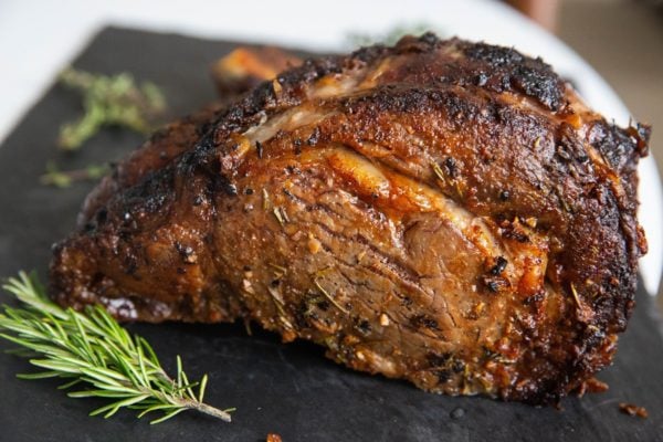 Finished prime rib sitting on a cutting board with fresh herbs to the side.