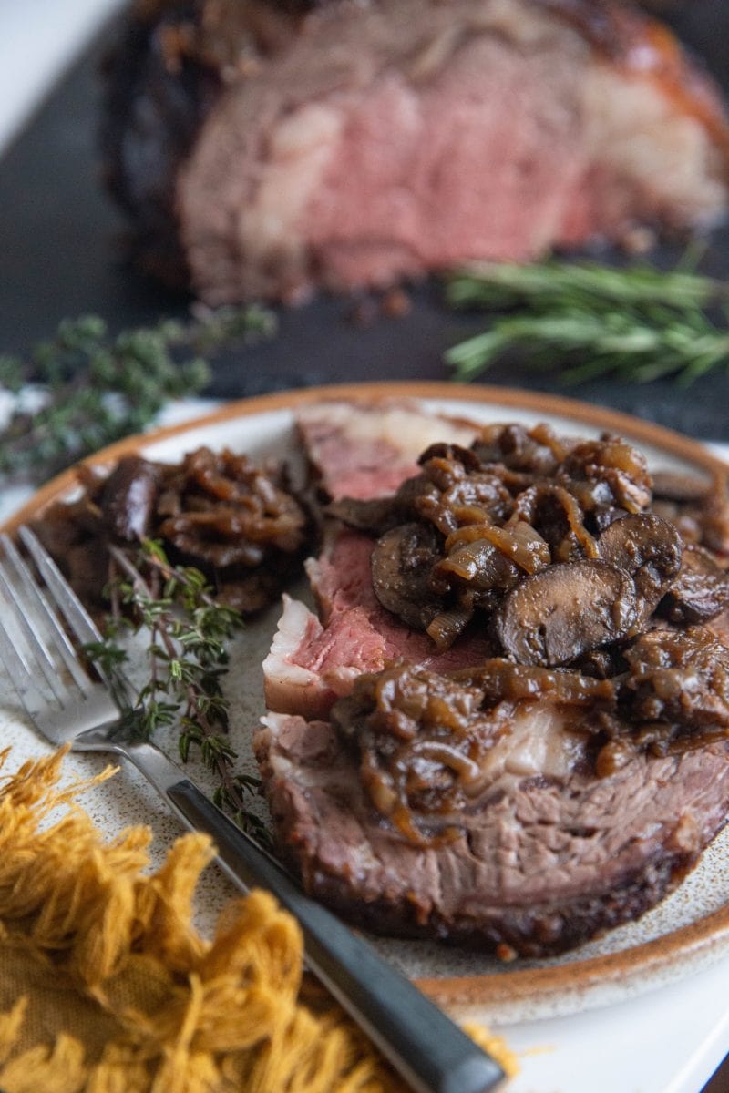 Prime rib steak on a plate with sauteeed mushrooms and onions.