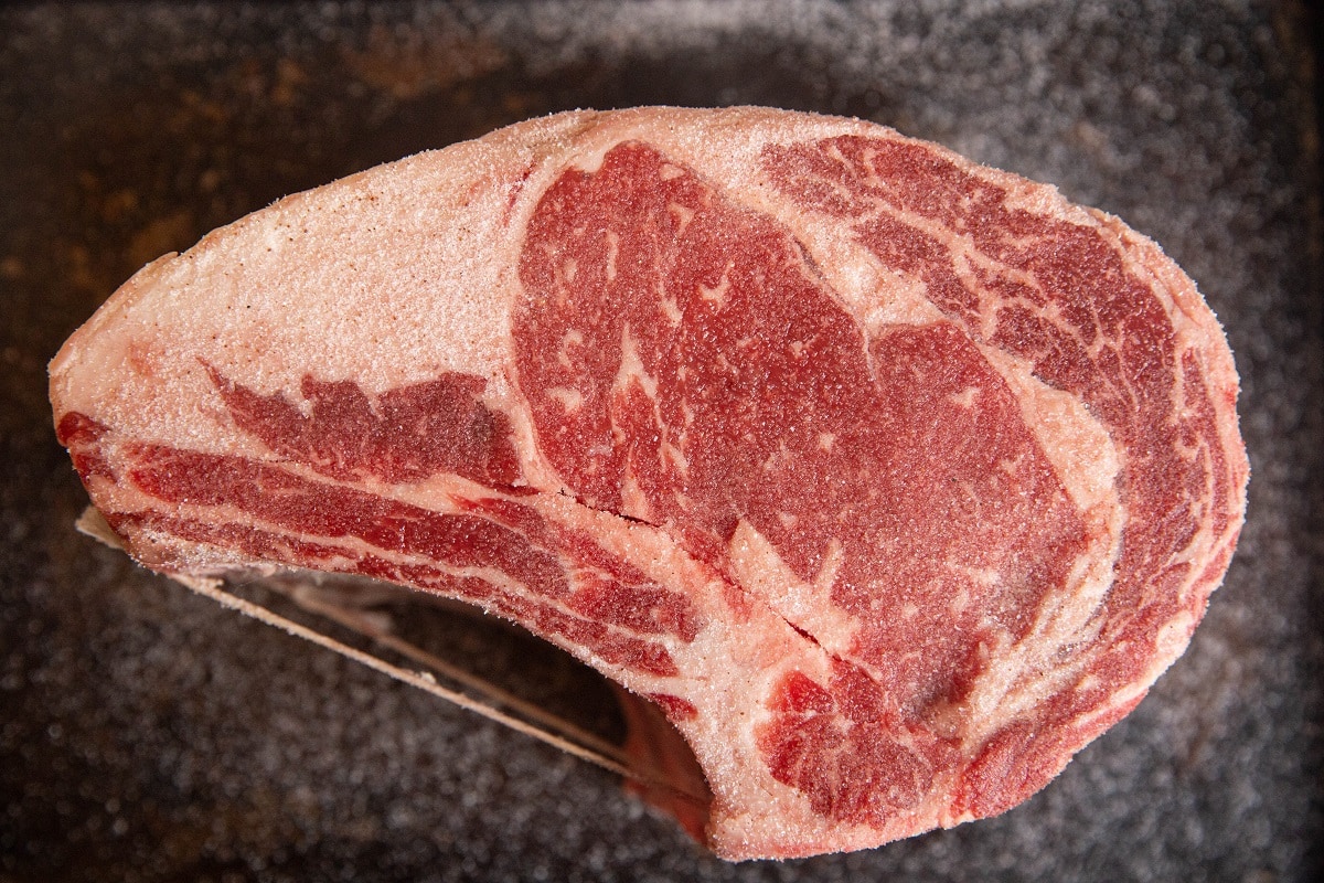 bone-in prime rib roast sitting on a baking sheet sprinkled with salt for a dry brine.