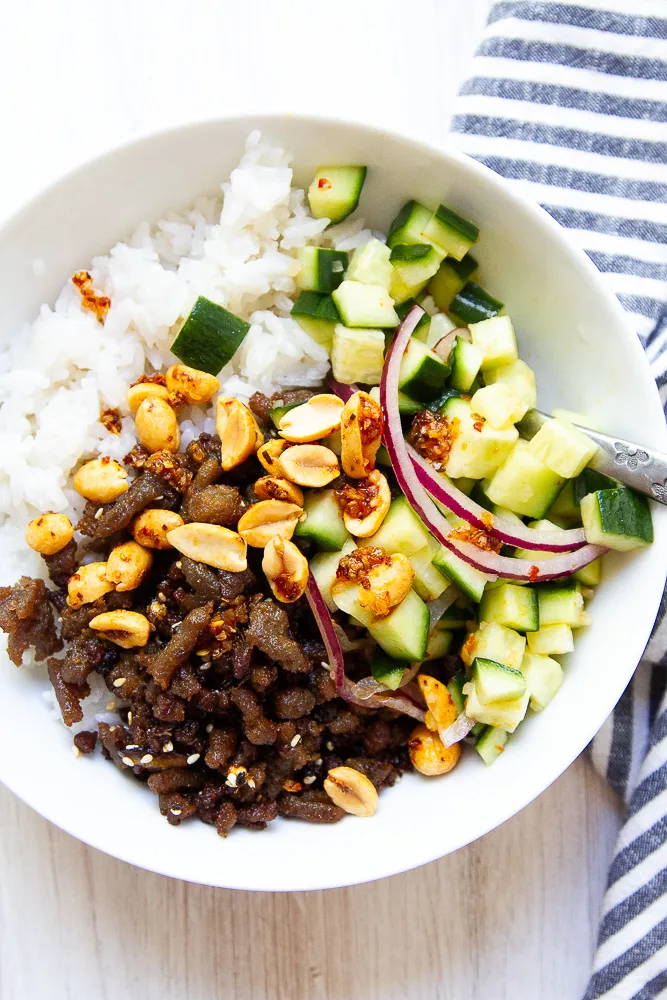 Bowl of spicy ground turkey with rice and pickled cucumbers and peanuts on top.