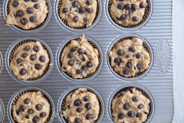 Muffin tin lined with muffin papers, filled with banana muffin batter.