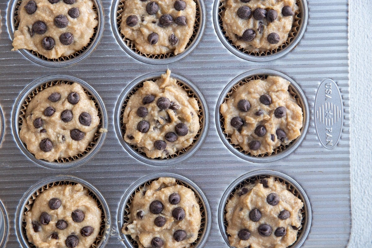 Muffin tin lined with muffin papers, filled with banana muffin batter.