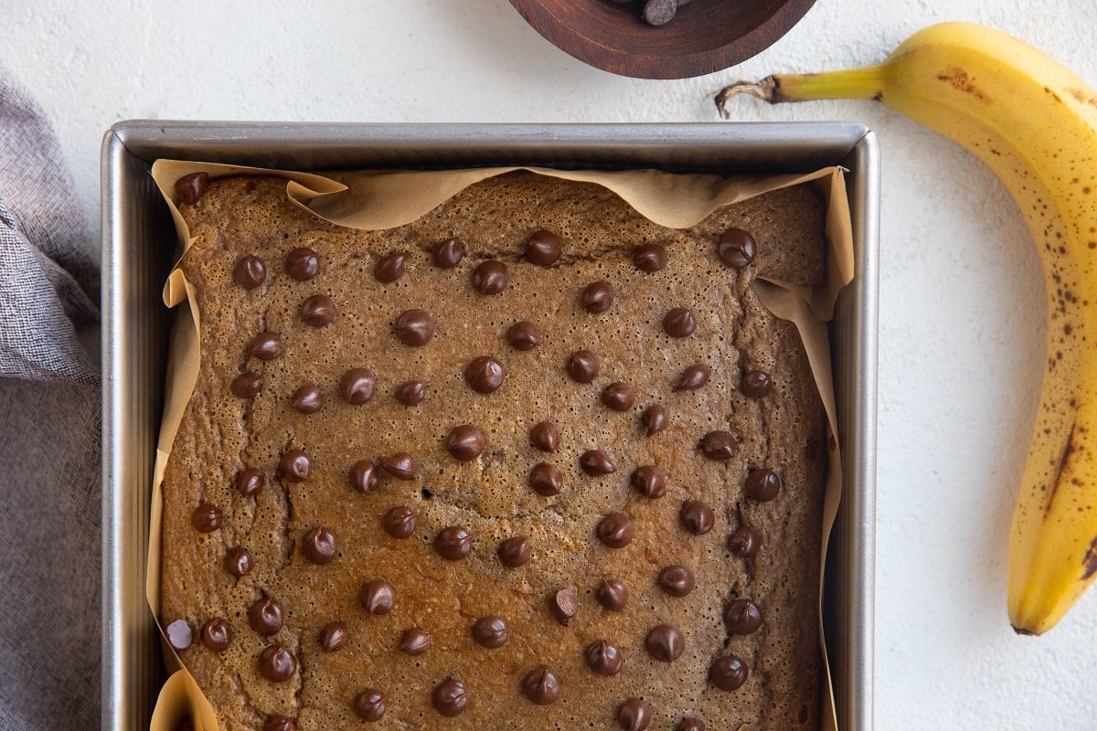 Horizontal image of baked oats in a square pan with a ripe banana to the side.