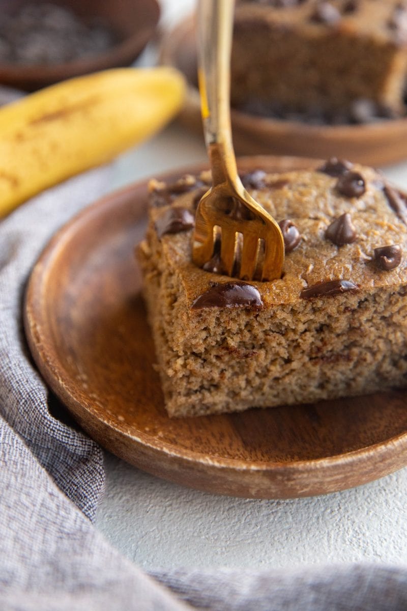 Slice of baked oatmeal on a wooden plate with a fork taking a bite out.