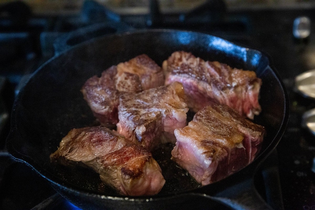 Large chunks of beef searing in a cast iron skillet