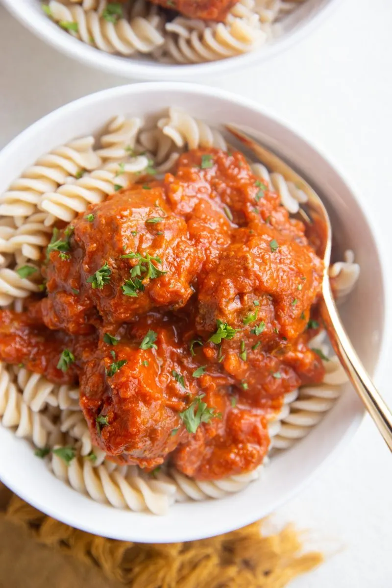 Two white bowls of pasta with meatballs and sauce on top with gold forks.