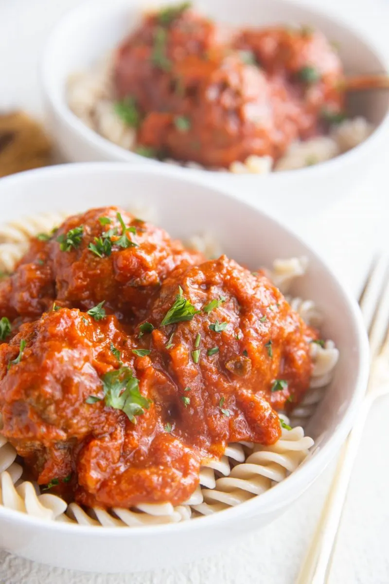 Angle shot of two white bowls of pasta with meatballs on top, ready to eat.