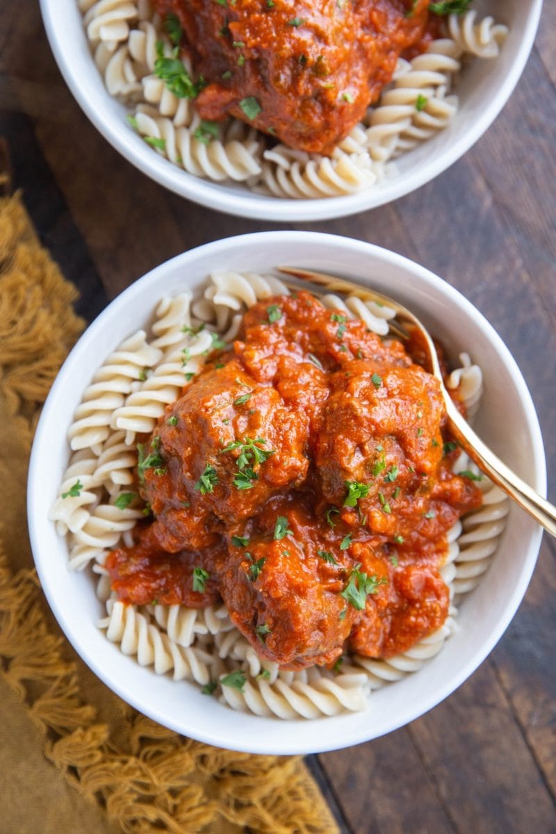 Top down image of two bowls of meatball pasta on a rustic wood backdrop.