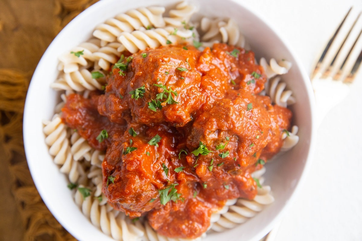 Horizontal photo of a white bowl full of pasta and meatballs with red sauce.