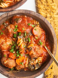 Two wooden bowls of meatball soup on a white background