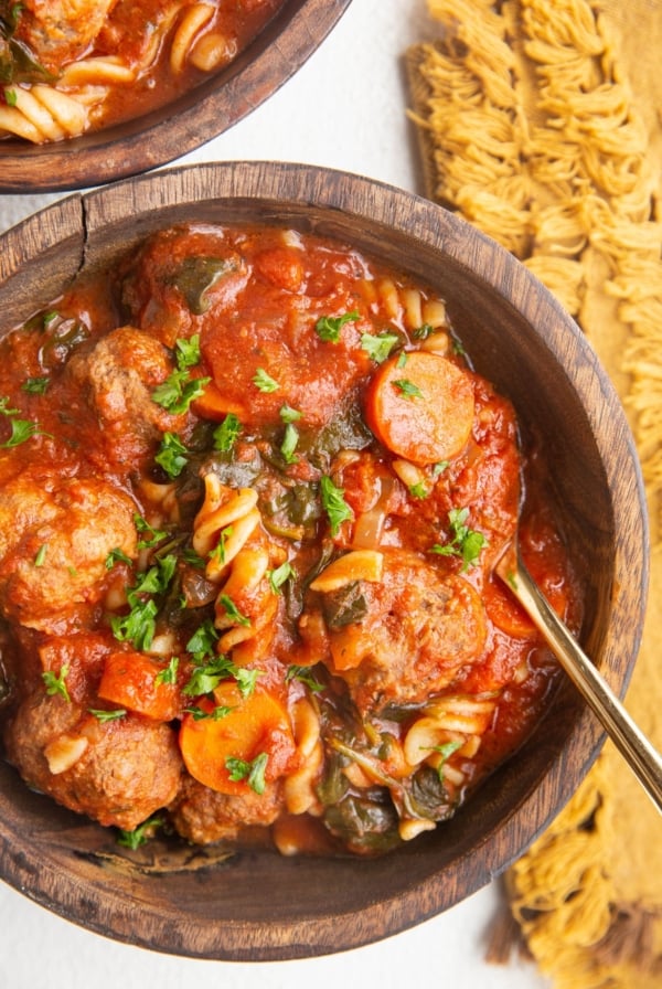 Two wooden bowls of meatball soup on a white background