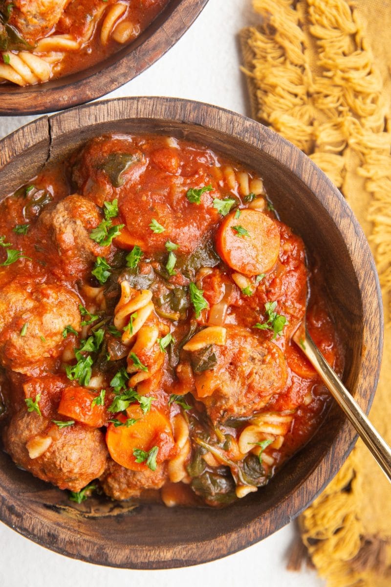 Two wooden bowls of meatball soup on a white background