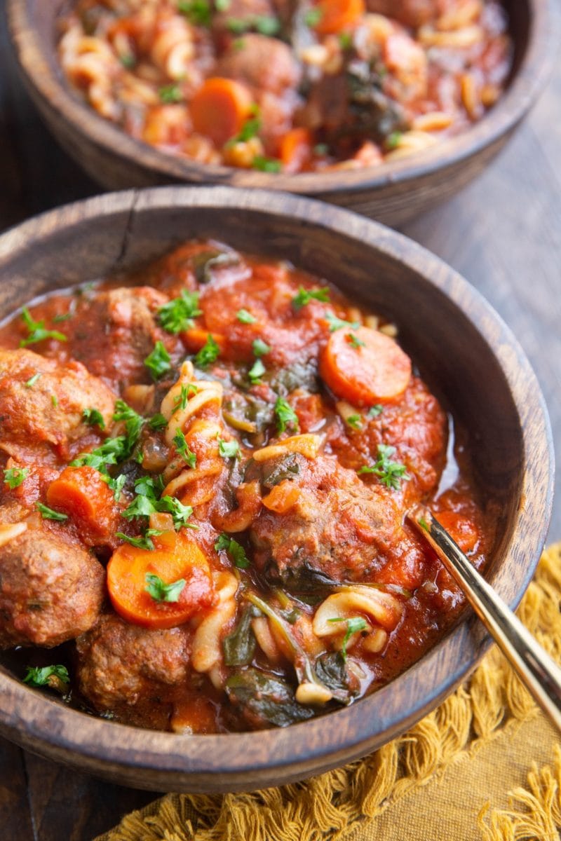 Two bowls of meatball soup on a wood background.