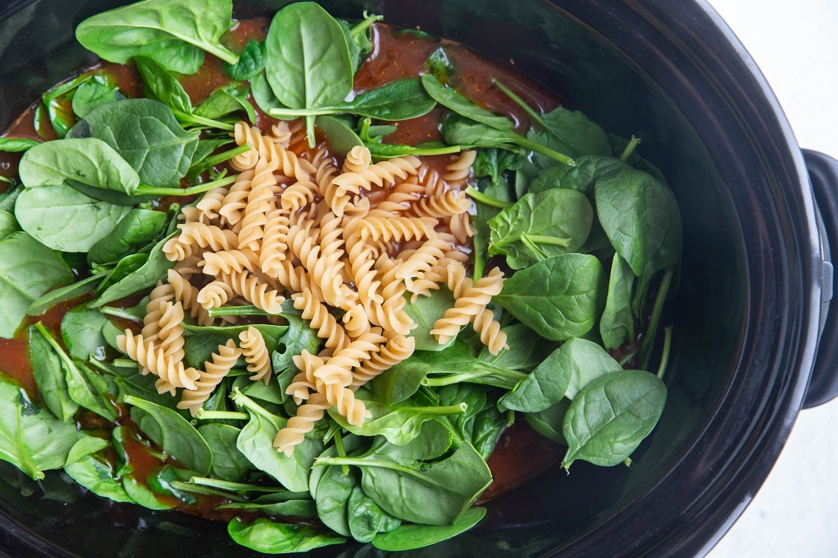 Spinach and un cooked pasta being stirred into the soup.