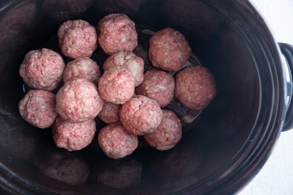 Raw meatballs at the bottom of a slow cooker, ready to be cooked.