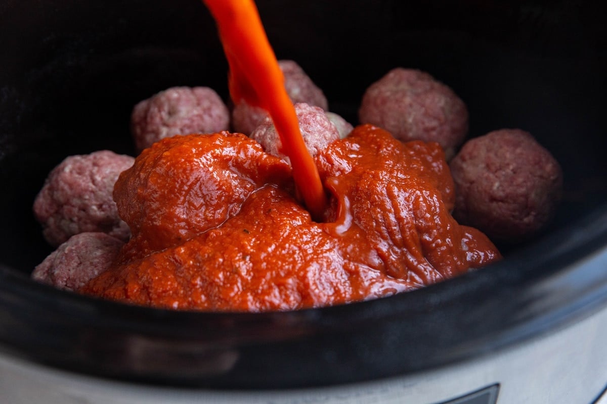 Pouring tomato sauce into the crock pot with the meatballs.