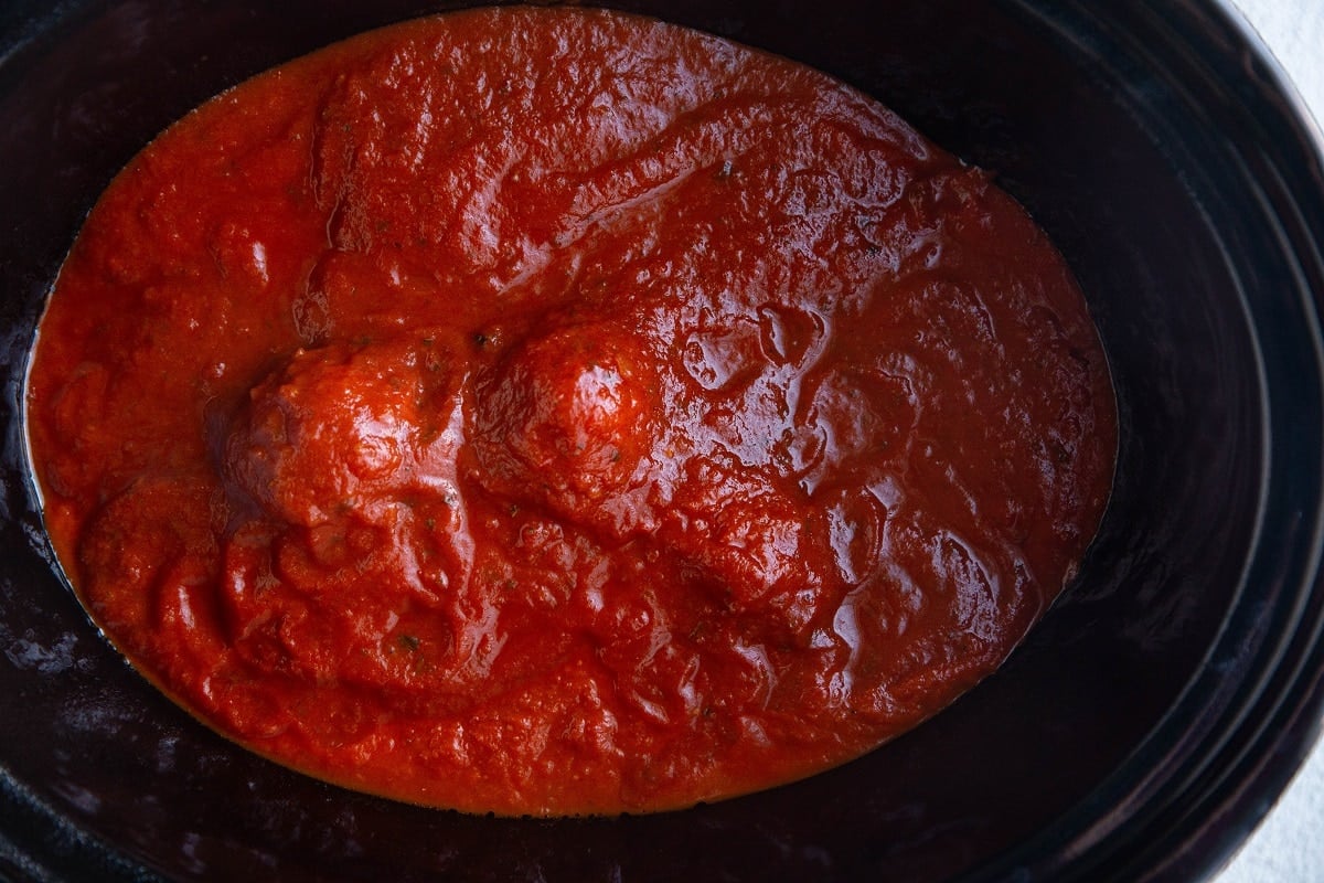 Crock pot with sauce and meatballs inside, ready to be cooked.