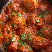 Angle shot of Italian meatballs in a crock pot, sprinkled with fresh parsley.