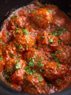 Angle shot of Italian meatballs in a crock pot, sprinkled with fresh parsley.