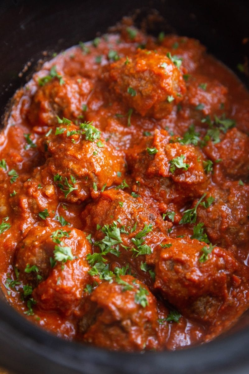 Angle shot of Italian meatballs in a crock pot, sprinkled with fresh parsley.